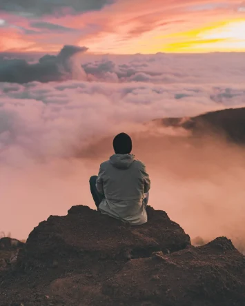Person sitting on a mountain above clouds.