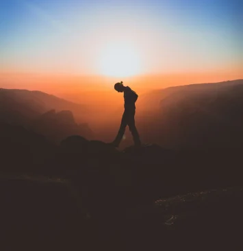 Silhouette of a person standing on a mountain at sunrise.
