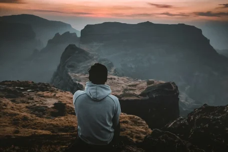 Person sitting on a cliff overlooking mountains